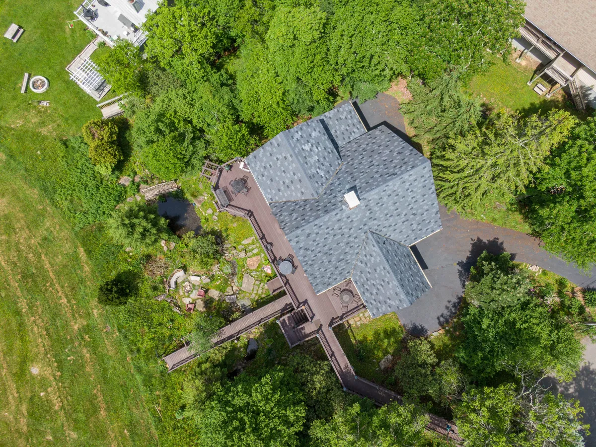 An exterior view of the house showcases the landscaped garden, winding pathways, and the connection to the deck. The image captures the architectural integration of the garage area, with a visible deck walkway leading toward the surrounding nature—suggesting seamless access to outdoor adventure.