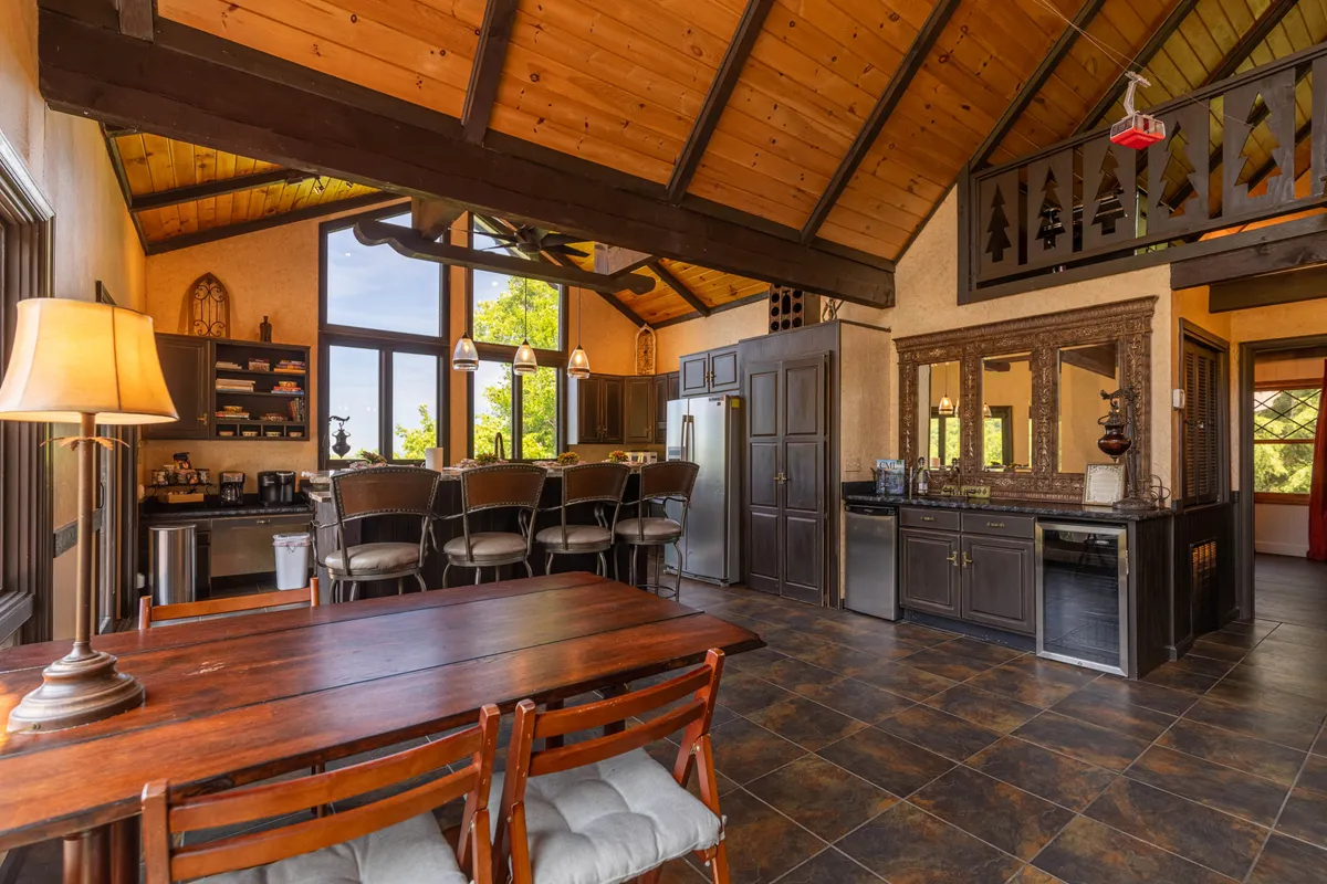 A dining area adjacent to the kitchen, featuring a large table for group meals, a kitchen island, wooden beams, and large windows that fill the space with light. The layout supports easy movement between spaces, ideal for group gatherings and entertaining.