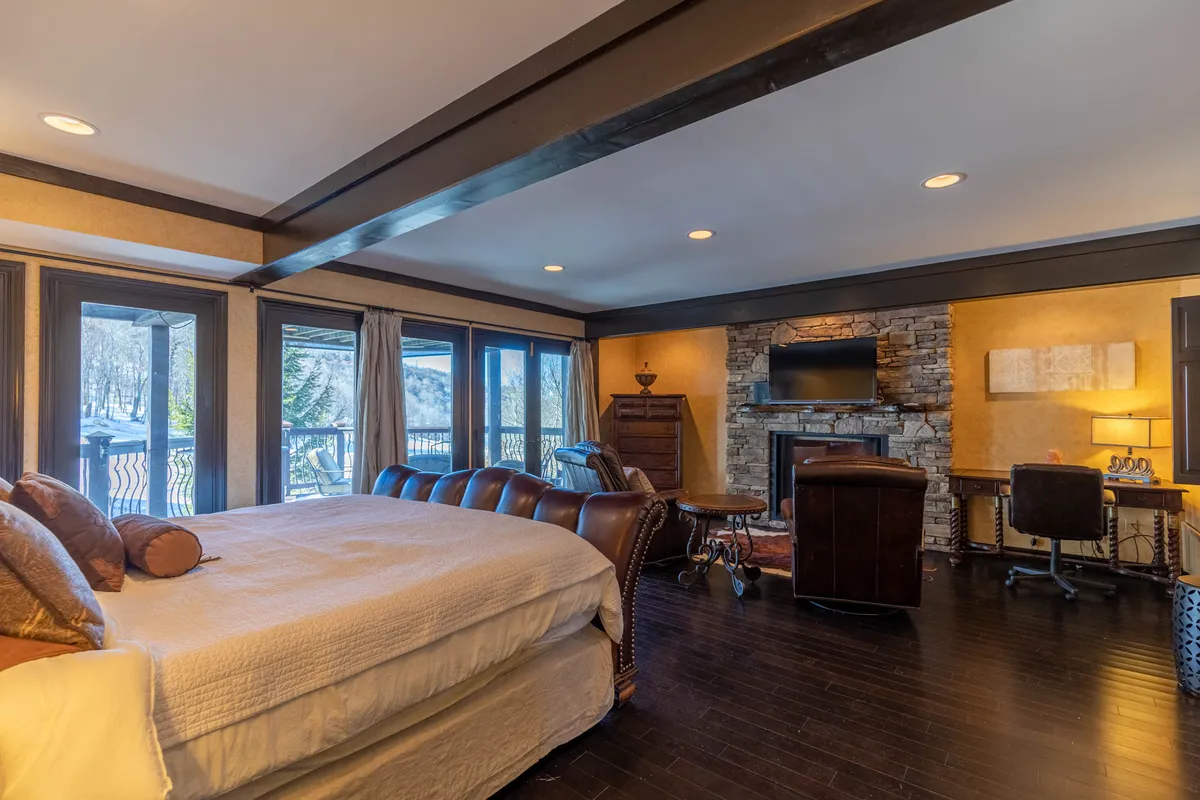 This image features a large bed positioned near windows that let in abundant natural light, accompanied by a stone fireplace for warmth and ambiance. The decor is comfortable and serene, creating a perfect setting for relaxation and restful sleep.