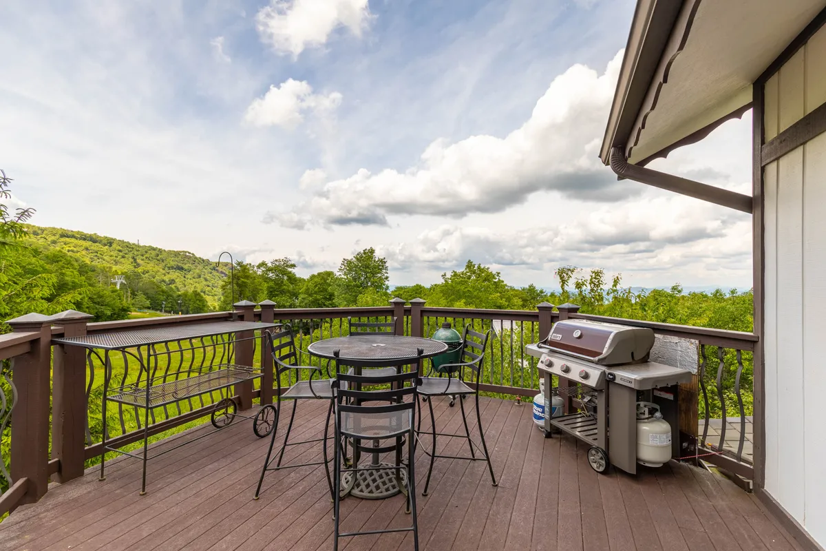 This exterior image shows a large dining table and chairs on a deck with grills (Weber and Green Egg) and panoramic mountain scenery. The atmosphere is casual, perfect for alfresco dining, barbecues, and gatherings.